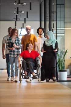 people walking a corridor in the glass-enclosed office of a modern startup, including a person in a wheelchair and a woman wearing a hijab.