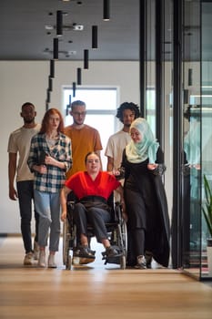 people walking a corridor in the glass-enclosed office of a modern startup, including a person in a wheelchair and a woman wearing a hijab.