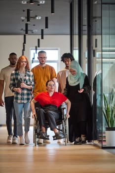 people walking a corridor in the glass-enclosed office of a modern startup, including a person in a wheelchair and a woman wearing a hijab.