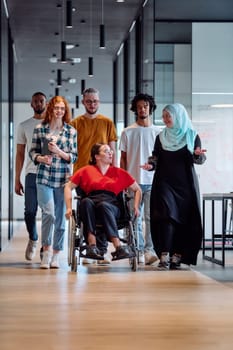 people walking a corridor in the glass-enclosed office of a modern startup, including a person in a wheelchair and a woman wearing a hijab.