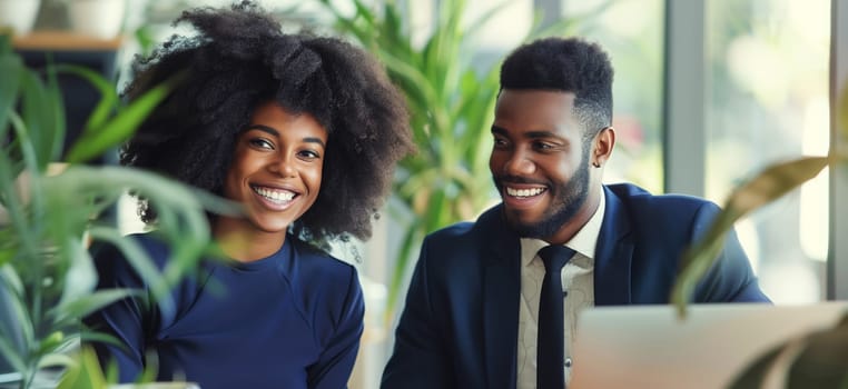 Happy smiling business people discussing a new project together sitting at the desk with laptop in an office, cheerful african colleagues having a conversation at a meeting