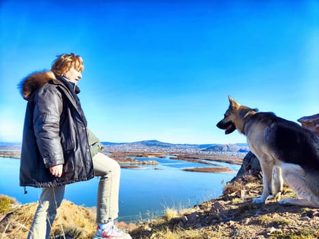 Adult girl with shepherd dog taking selfie near water of lake or river in mountain. Middle aged woman and big pet on nature. Friendship, love and fun