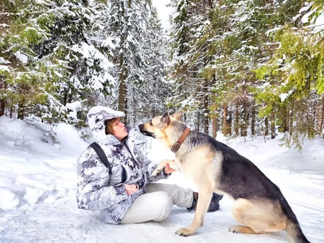 Adult girl or mature lady with shepherd dog in winter nature landscape in forest. Middle aged woman training big shepherd dog in cold day. Friendship, love, communication, fun, hugs