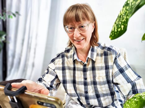 Smiling woman in glasses using a smartphone on a tripod for a video chat. A middle-aged woman posing and taking a selfie