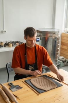 A potter cuts a piece of rolled clay with patterns. Vertical photo
