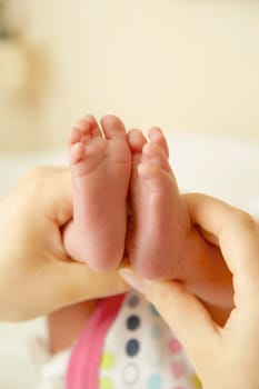 Mom holds the baby's legs in her hands, touches the newborn's feet with love, close-up. A mother's love for her baby.