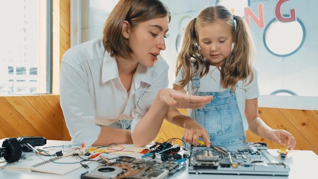 Young smart caucasian teacher teaching students about part of electronic board. Expert girl learn about digital electrical tool and fixing motherboard at table with chips and wires placed. Erudition.