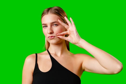 Young Woman Gesturing Silence With Finger on Lips Against Green Screen Background in studio