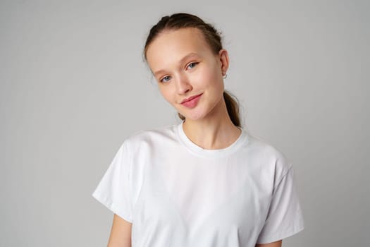 Beautiful young girl posing in white T-shirt and jeans on gray background in studio