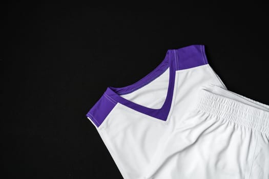 A close-up view of a white and purple athletic tank top neatly arranged on a dark background, highlighting its sporty design and contrasting vibrant trim. The fabric texture suggests a focus on breathability and performance, suitable for sportswear.