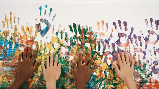 Happy diverse student hand placed on colorful stained wall. Closeup of multicultural hand or children with mixed races paint their hand print at art room. Background. Creative activity. Edification.