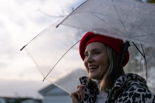 A woman is smiling under a clear umbrella. She is wearing a red hat and a black and white jacket