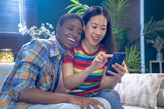 Two young beautiful smiling girls looking on the phone together happy, in a living room. High quality photo