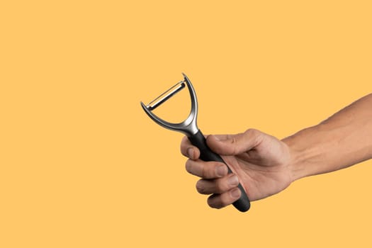 Black male hand holding a potato peeler isolated on yellow background. High quality photo