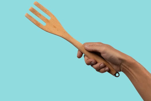 Hand holding wooden fork on cyan background cutout. High quality photo