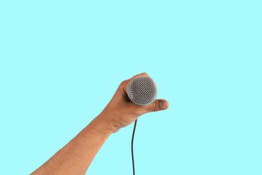 Black male singer hand holding a microphone isolated on cyan background. High quality photo