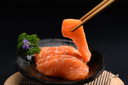Japanese food, Salmon sashimi with parsley leaf on black plate.