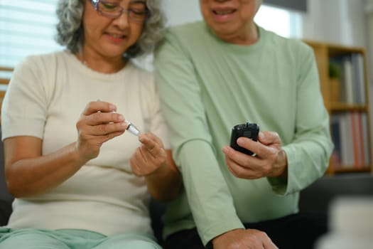 Smiling mature woman checking blood sugar level by glucometer at home. Diabetes and health care concept.