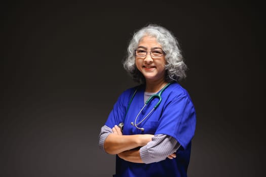 Friendly senior woman doctor standing against black background. Medicine and health care concept.