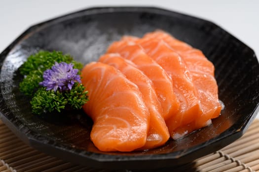 Close up sliced salmon with parsley leaf in black plate. Japanese food style.