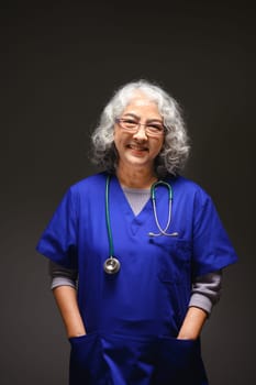 Portrait of gray haired mature female doctor standing on black background. Medical careers concept.