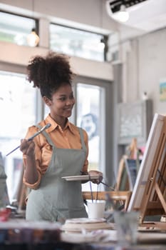 A young black artist paints acrylic paints on canvas with determination in her painting studio.