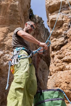 A man is climbing a rock wall with a rope tied to his waist. He is wearing a green shirt and pants