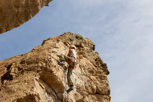 A woman is climbing a rock wall with a rope. Concept of adventure and excitement, as the man is taking on a challenging physical activity