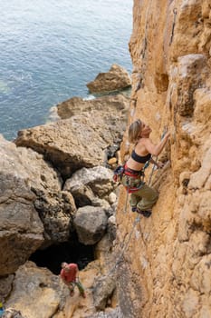A woman is climbing a rock wall while a man watches. The scene is exciting and adventurous, with the woman's determination and the man's support