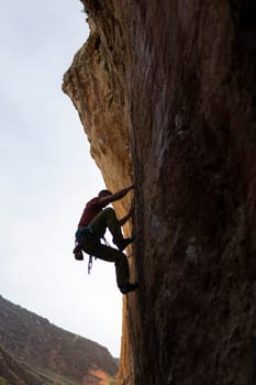 A person is climbing a rock wall in a cave. The cave is dark and the person is the only one in the scene