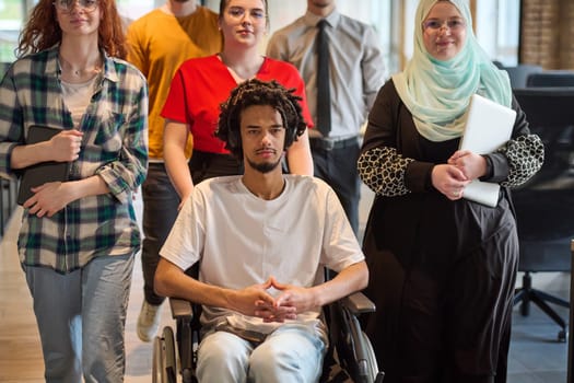 A diverse group of young business people congregates within a modern startup's glass-enclosed office, featuring inclusivity with a person in a wheelchair, an African American young man, and a hijab muslim woman