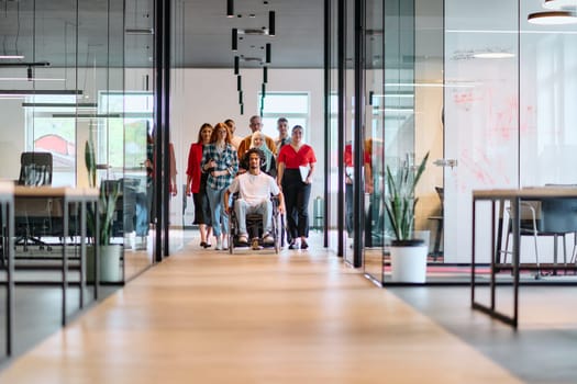 A diverse group of young business people walking a corridor in the glass-enclosed office of a modern startup, including a person in a wheelchair and a woman wearing a hijab.