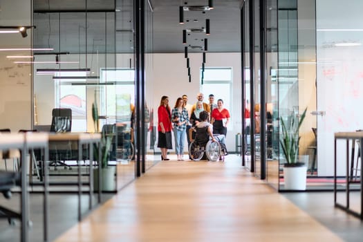 A diverse group of young business people walking a corridor in the glass-enclosed office of a modern startup, including a person in a wheelchair and a woman wearing a hijab.