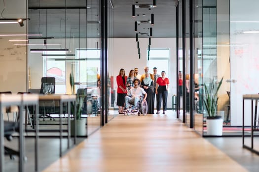 A diverse group of young business people walking a corridor in the glass-enclosed office of a modern startup, including a person in a wheelchair and a woman wearing a hijab.