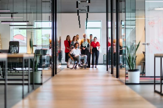 A diverse group of young business people walking a corridor in the glass-enclosed office of a modern startup, including a person in a wheelchair and a woman wearing a hijab.