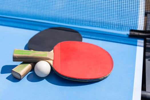 Red and black Table Tennis Paddles and ball on the blue table tennis table with net. Ping Pong concept with copy space. High quality photo