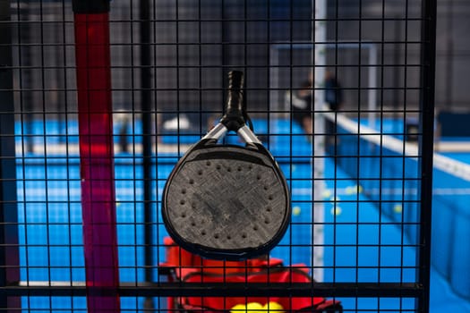 Black professional paddle tennis racket and ball with natural lighting on blue background. Horizontal sport theme poster, greeting cards, headers, website and app. High quality photo