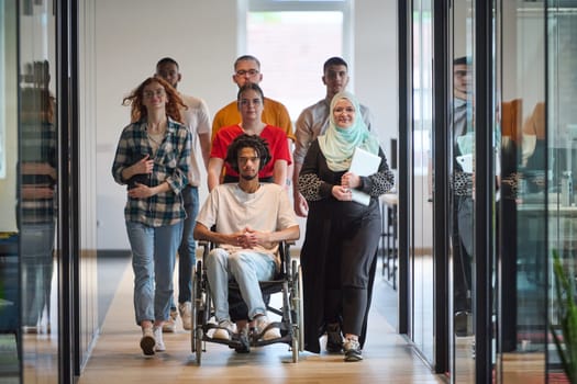 A diverse group of young business people congregates within a modern startup's glass-enclosed office, featuring inclusivity with a person in a wheelchair, an African American young man, and a hijab muslim woman