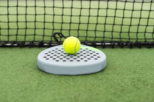 Padel racket and padel ball on a green court in the sunset. High quality photo