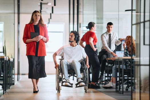 A business leader with her colleague, an African-American businessman who is a disabled person, pass by their colleagues who work in modern offices.