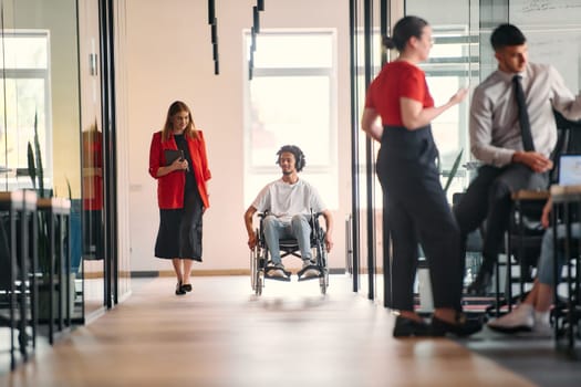 A business leader with her colleague, an African-American businessman who is a disabled person, pass by their colleagues who work in modern offices.