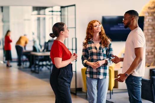 A group of young business individuals, including a girl with orange hair and an African American man, stands in a modern corporate hallway, collectively examining business progress on a smartphone, exemplifying dynamic collaboration and digital engagement