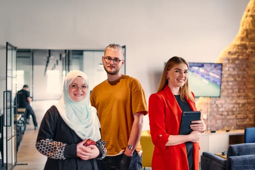 A group of young business colleagues, including a woman in a hijab, stands united in the modern corridor of a spacious startup coworking center