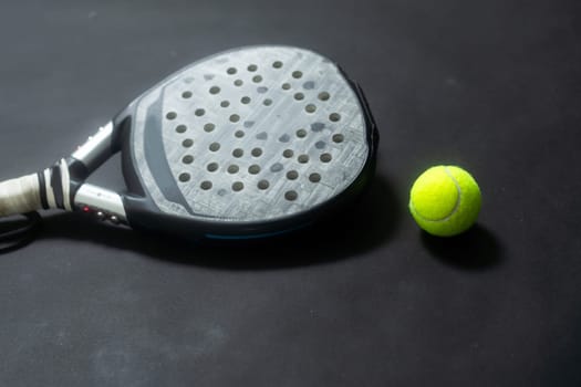 Detailed background of black and white padel racket and ball on black background. Top view. High quality photo
