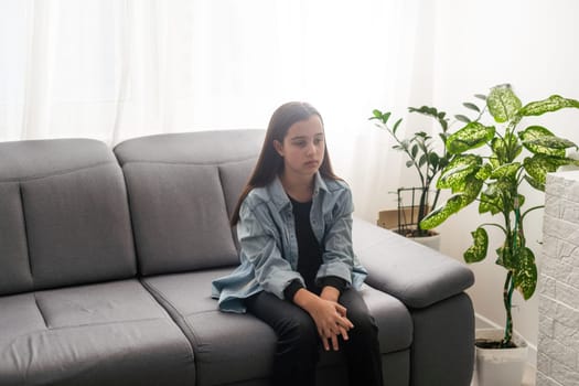 girl wearing blue shirt sitting on couch at home and looking away. Lifestyle child portrait. High quality photo