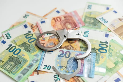 Police handcuffs lies on a set of green monetary denominations of 100 euros. A lot of money forms an infinite heap. High quality photo