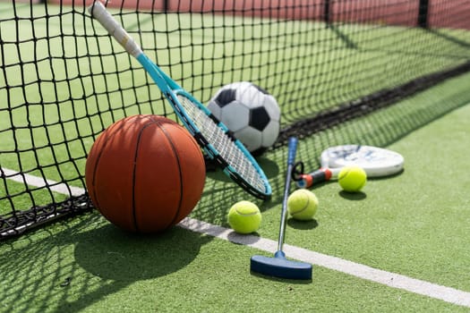 A variety of sports equipment including an american football, a soccer ball, a tennis racket, a tennis ball, and a basketball. High quality photo