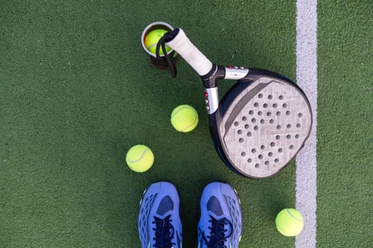 Yellow balls on grass turf near padel tennis racket behind net in green court outdoors with natural lighting. Paddle is a racquet game. Professional sport concept with copy space. High quality photo
