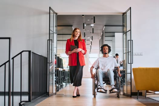 A business leader with her colleague, an African-American businessman who is a disabled person, pass by their colleagues who work in modern offices.