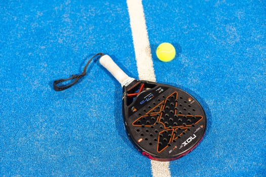 Kyiv, Ukraine, April 18, 2024. Black professional paddle tennis racket and ball with natural lighting on blue background. Horizontal sport theme poster, greeting cards, headers, website and app. High quality photo